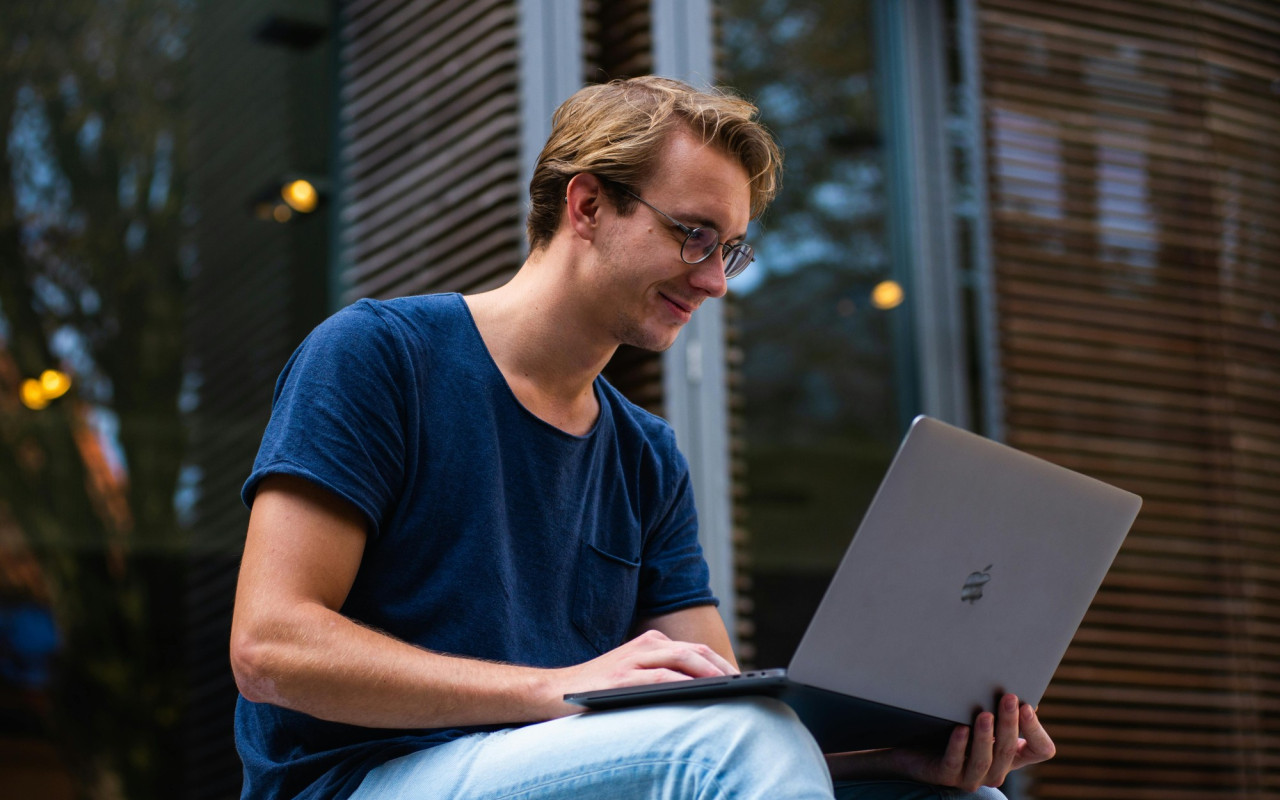 Young man smiling at his laptop, outdoor setting